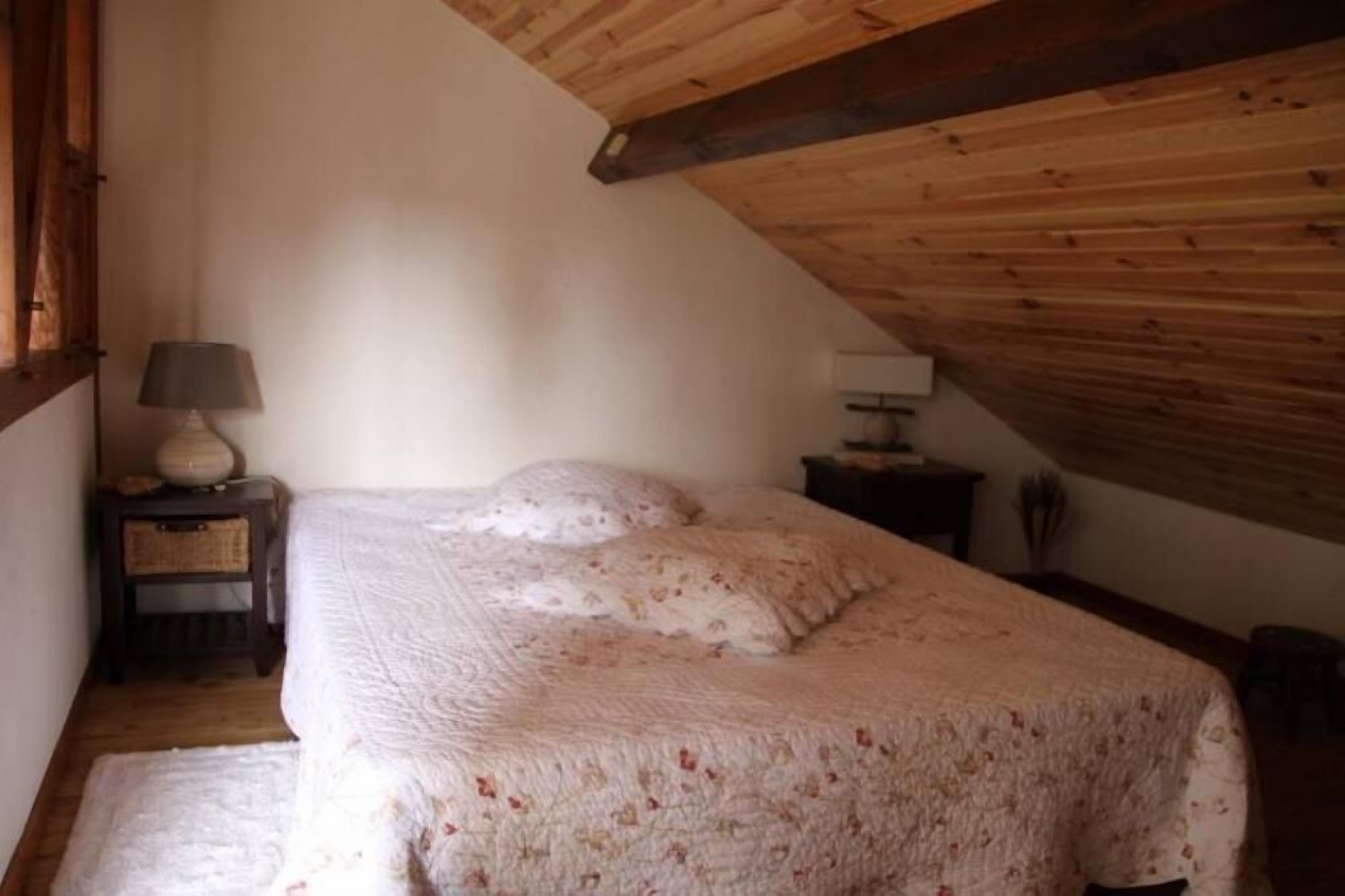 Ein Schlafzimmer mit Holzbalkendecke, einem Bett mit floralem Überwurf, einer Nachttischlampe und einem kleinen Nachttisch.