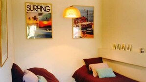 A room with two single beds, a wall-mounted lamp, and two framed pictures depicting surfing scenes. - Accommodation near the sea with 100m2 fenced garden. Closed private parking with beeper. (La Ciotat)
