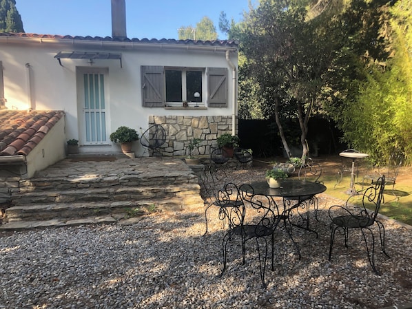 A rustic house with a stone staircase leading to a door, surrounded by a gravel patio with metal chairs and tables.