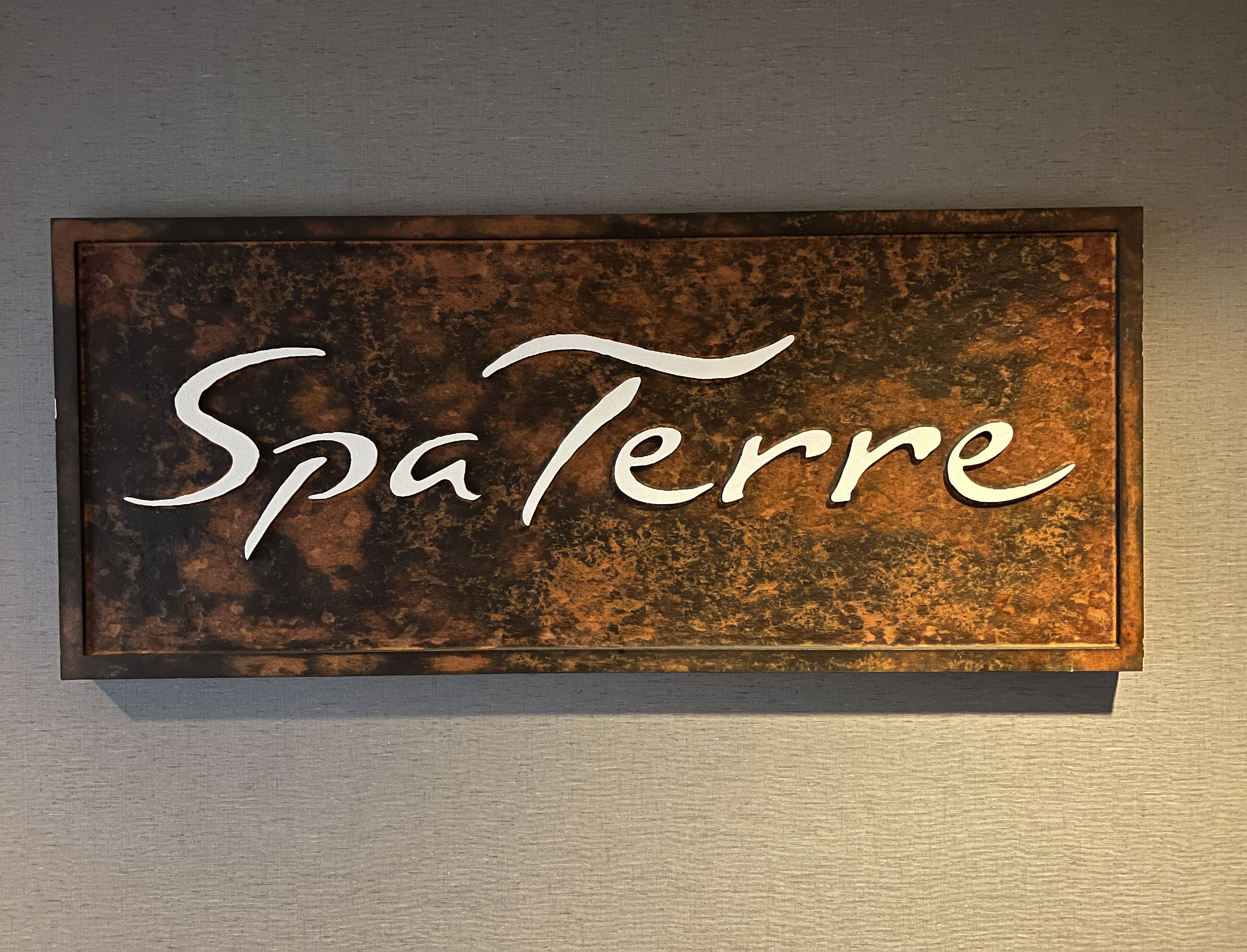 Ein Schild mit dem Schriftzug 'Spa Terre' vor einem strukturierten Hintergrund.