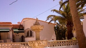 A multi-tiered stone fountain with sculptures, set against a white wall with a decorative fence, palm trees, and a clear sky. - Lovely modern 2 bed apartment sleeps 4 FREE WiFi A/C, TV, private Pool & parking (Teulada)