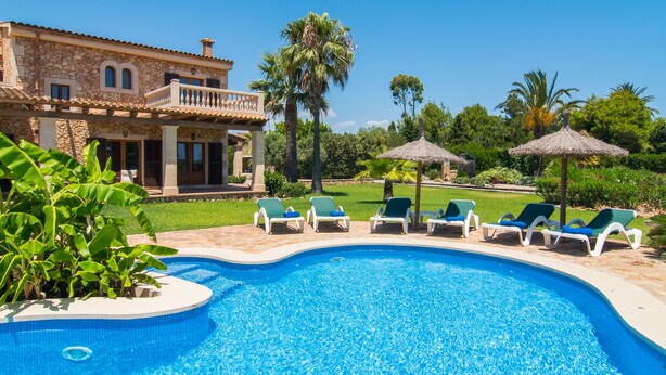 Una piscina con sillones de descanso y una casa al fondo.