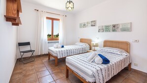 Una habitación con dos camas, una silla, un ventanal con cortinas y decoración en la pared.