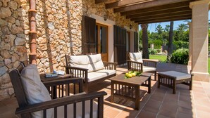 Un patio al aire libre con muros de piedra, mobiliario de madera y vista a un jardín ajardinado.
