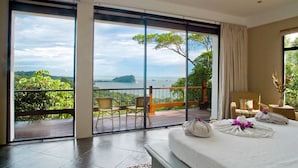 A bedroom with a large sliding glass door leading to a balcony with a view of a body of water and greenery. - Balinese Style Tropical Villa w/4 suites Huge Ocean Views Private Pool  (Manuel Antonio)