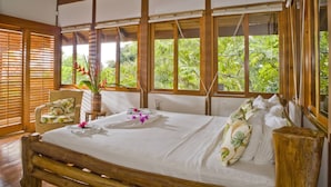 A spacious room with a large bed, wooden beams, and large windows offering a view of lush greenery. - Balinese Style Tropical Villa w/4 suites Huge Ocean Views Private Pool  (Manuel Antonio)