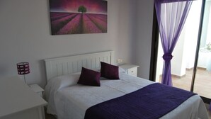 A bedroom with a white bed, purple bedding, a nightstand with a lamp, and a painting of a field with a tree. - Apartment  in Alcaidesa (Alcaidesa)