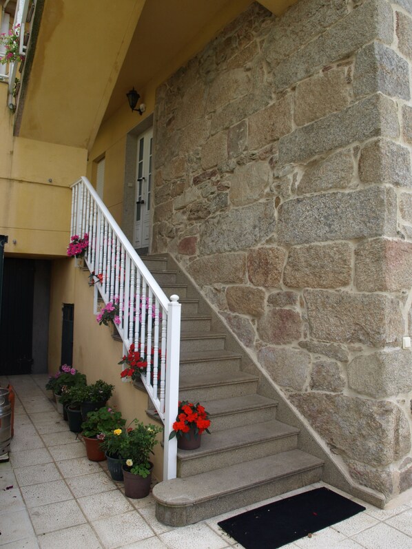 Una escalera de piedra con barandilla blanca que lleva a una puerta, rodeada de macetas con plantas y flores.