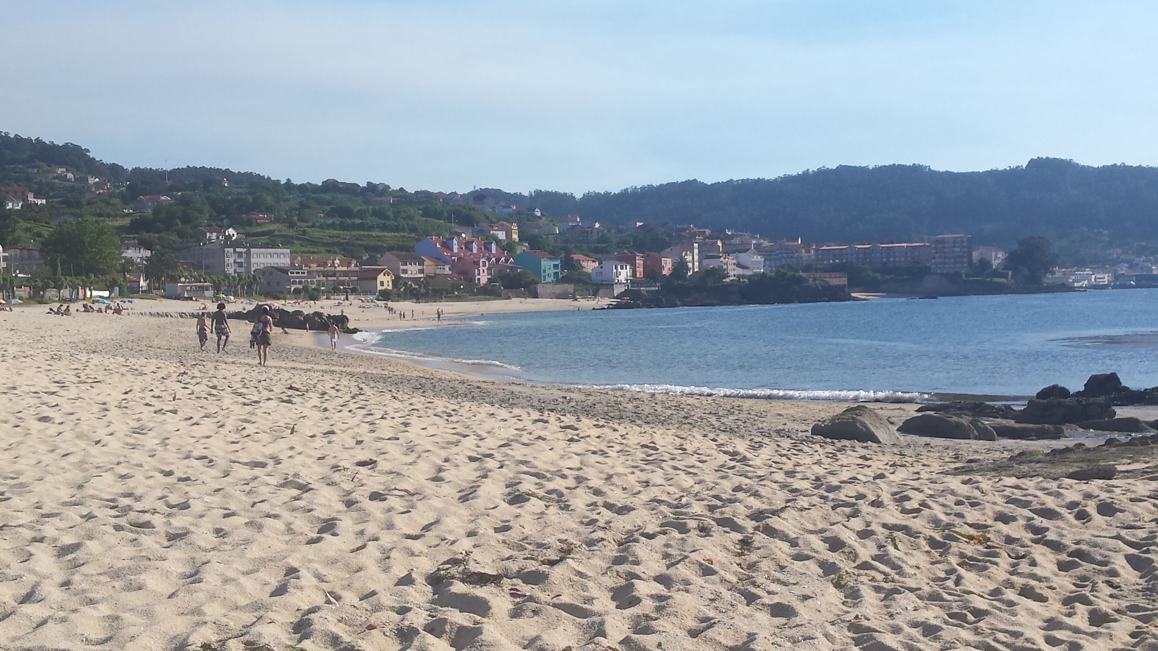 A sandy beach with footprints, a few people, and buildings in the background.