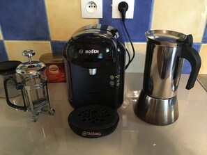 Uma cafeteira, uma prensa francesa e um bule de aço inoxidável em uma bancada de cozinha.
