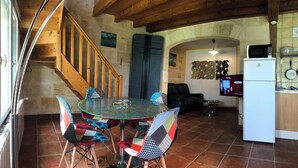 A cozy kitchen with a dining area, wooden staircase, and a TV displaying a home shopping channel. - Gîtes La Glycine facing the Saint-Emilion river (Vignonet)