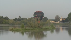 A hot air balloon over a calm lake with trees and a building in the background. - Gîtes La Glycine facing the Saint-Emilion river (Vignonet)
