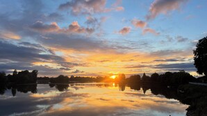A calm lake reflecting the sky during sunset with trees and a distant building. - Gîtes La Glycine facing the Saint-Emilion river (Vignonet)