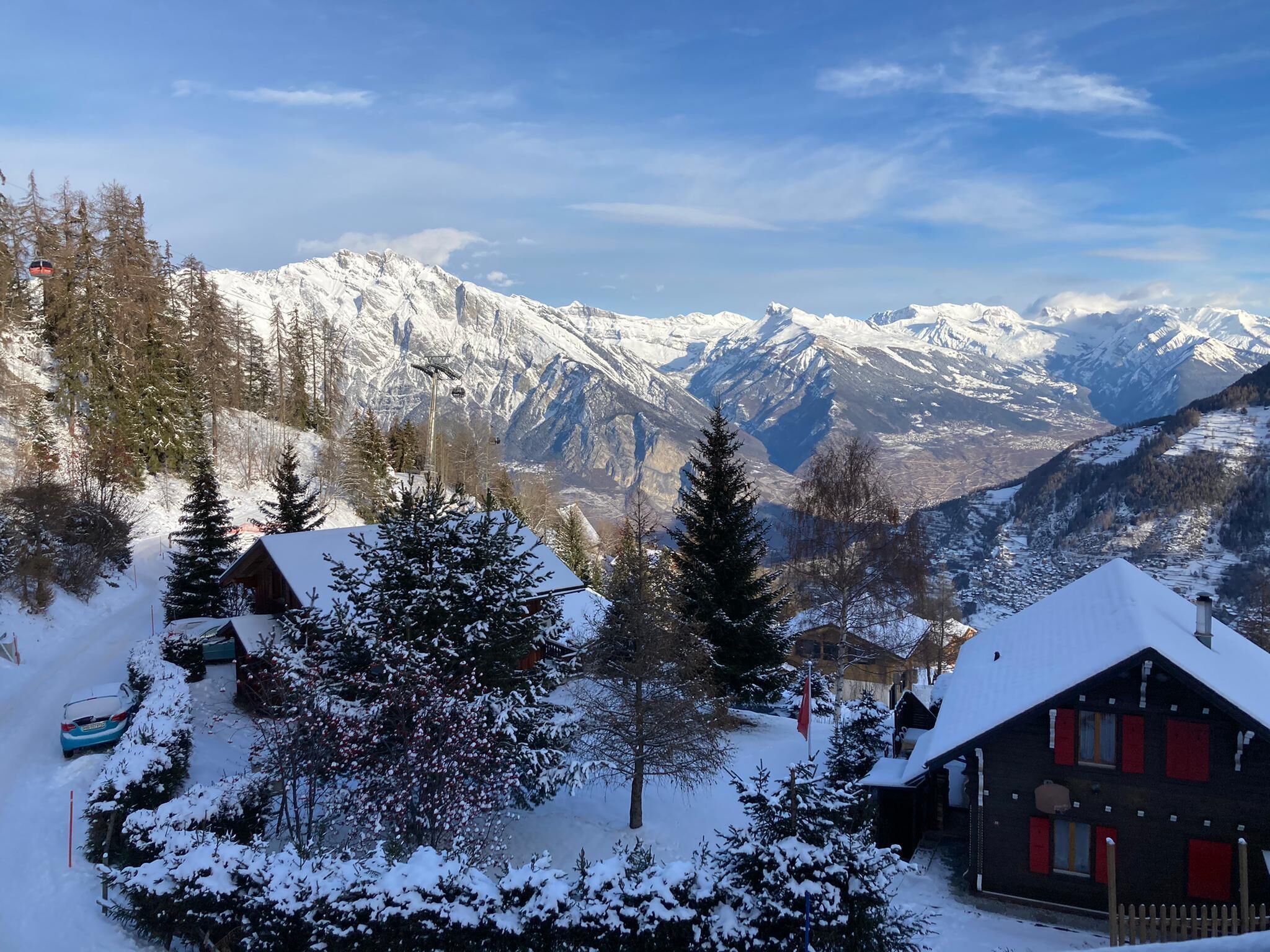 A snow-covered mountain village with traditional wooden houses, a ski lift, and a clear view of the surrounding peaks.