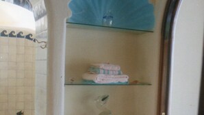 Un bagno con un mobiletto a vetro che contiene asciugamani piegati e un vaso decorativo.