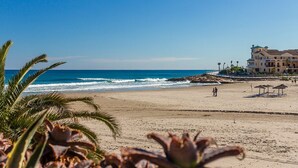 A beach with a building that has multiple balconies and a pool area.