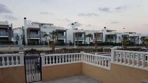 A rooftop terrace with a white balustrade, a black gate, and a view of modern buildings in the background.
