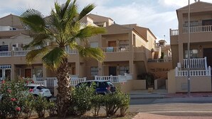 A residential building with balconies, a palm tree, and parked cars.