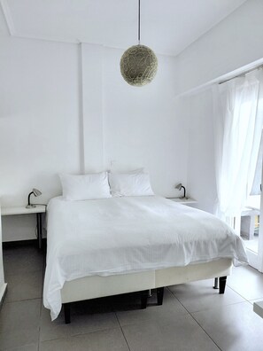 A minimalist bedroom with a large bed, bedside tables, and a hanging light fixture.