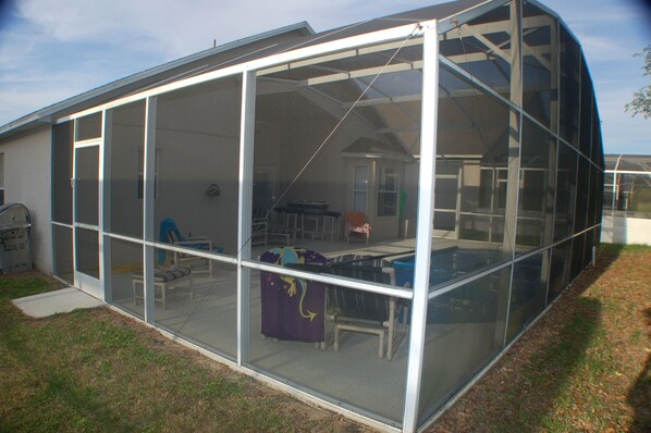 A house with a large enclosed patio area featuring a table and chairs, a covered seating area, and a visible garage.