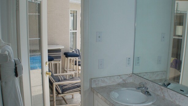 Et badeværelse med to håndvaske, et stort spejl og en dør, der fører ud til en balkon med en stol og et bord.