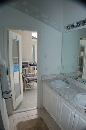 A bathroom with two sinks, a large mirror, and a door leading to a balcony with a chair and a table.