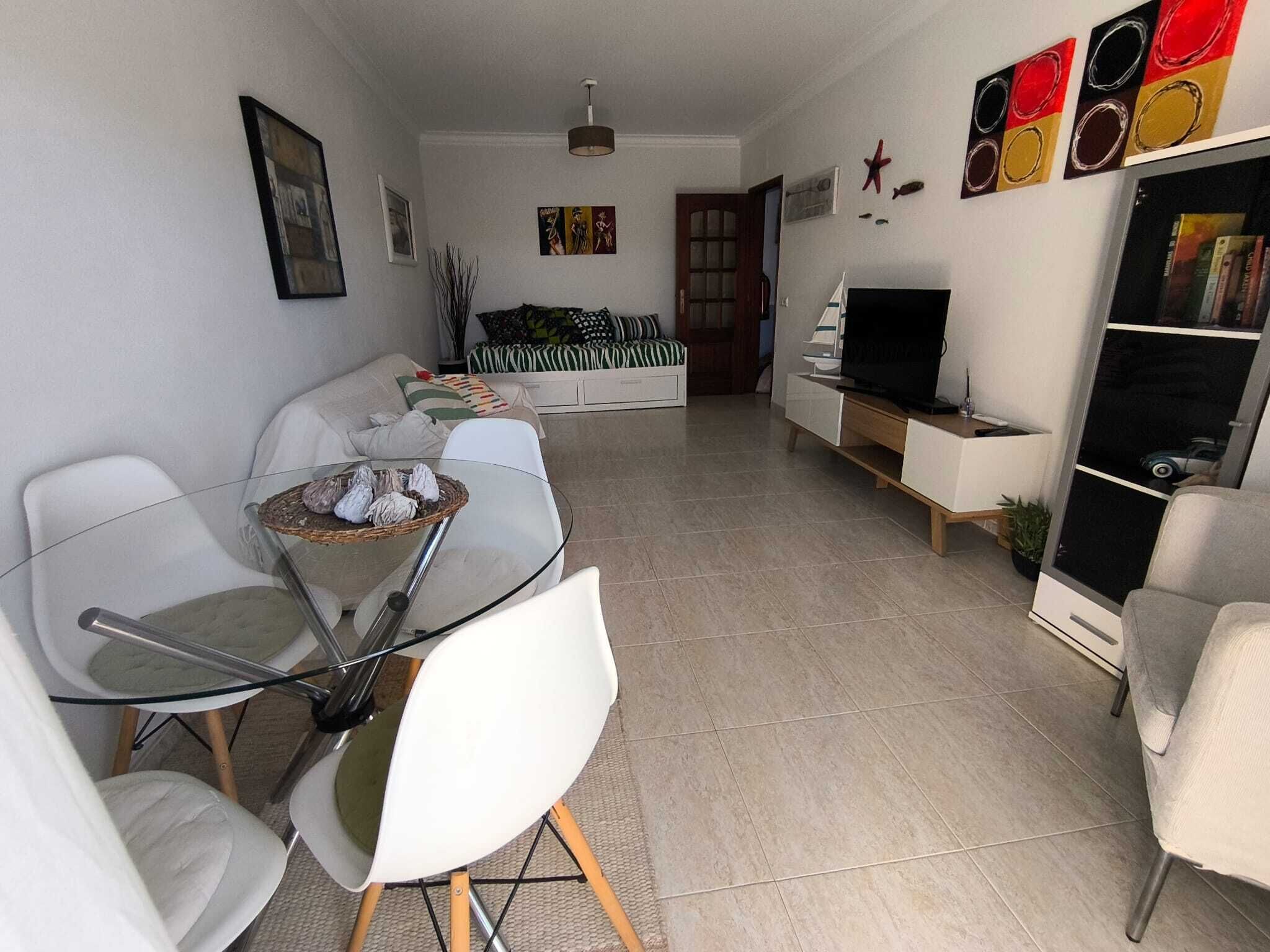 Un salon moderne avec une table à manger en verre, des chaises blanches, un canapé, un téléviseur et une bibliothèque.