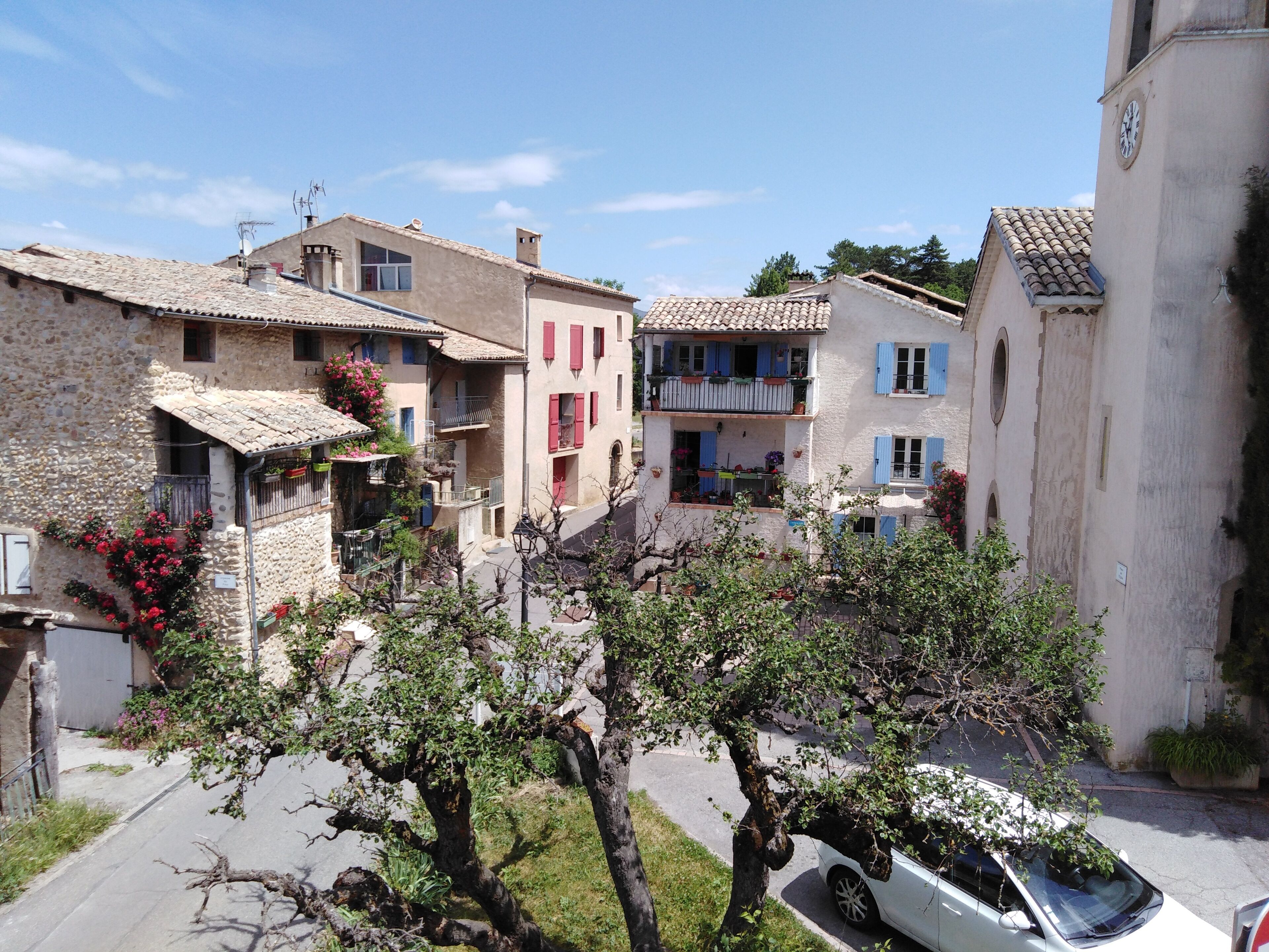 A row of traditional stone buildings with balconies, a narrow street, and a parked car.