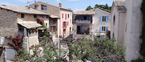 A row of traditional stone buildings with balconies, a narrow street, and a parked car.