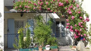 Ein Gebäude mit einem Balkon, der in Pink blüht, umgeben von verschiedenen Kübelpflanzen und einer hölzernen Bank.