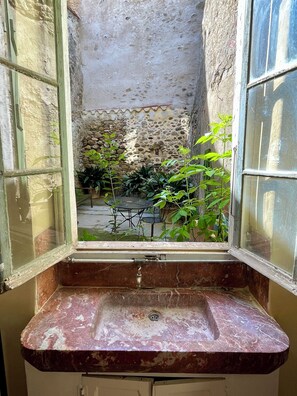 A bathroom with a marble sink, a window with a view of a stone wall and plants outside.