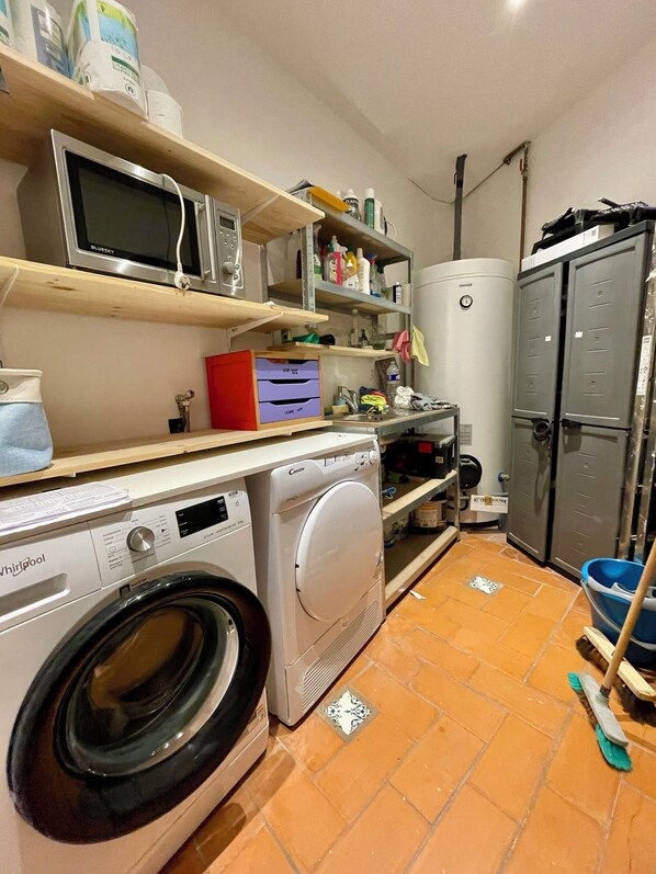 A laundry area with a washing machine, dryer, microwave, and shelves with various items.