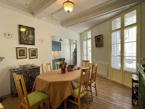 A dining room with a table set for four, wooden chairs, a vase with flowers, and a kitchen in the background.