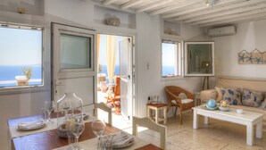 Amplia sala de estar con vista al mar, comedor con mesa dispuesta para dos personas y un rincón de descanso acogedor con sofá y sillones.