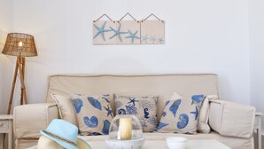 Un sofá beige con motivos de estrellas de mar y caracoles azules, un sombrero de paja, una vela en un candelabro y una lámpara sobre una mesita auxiliar.