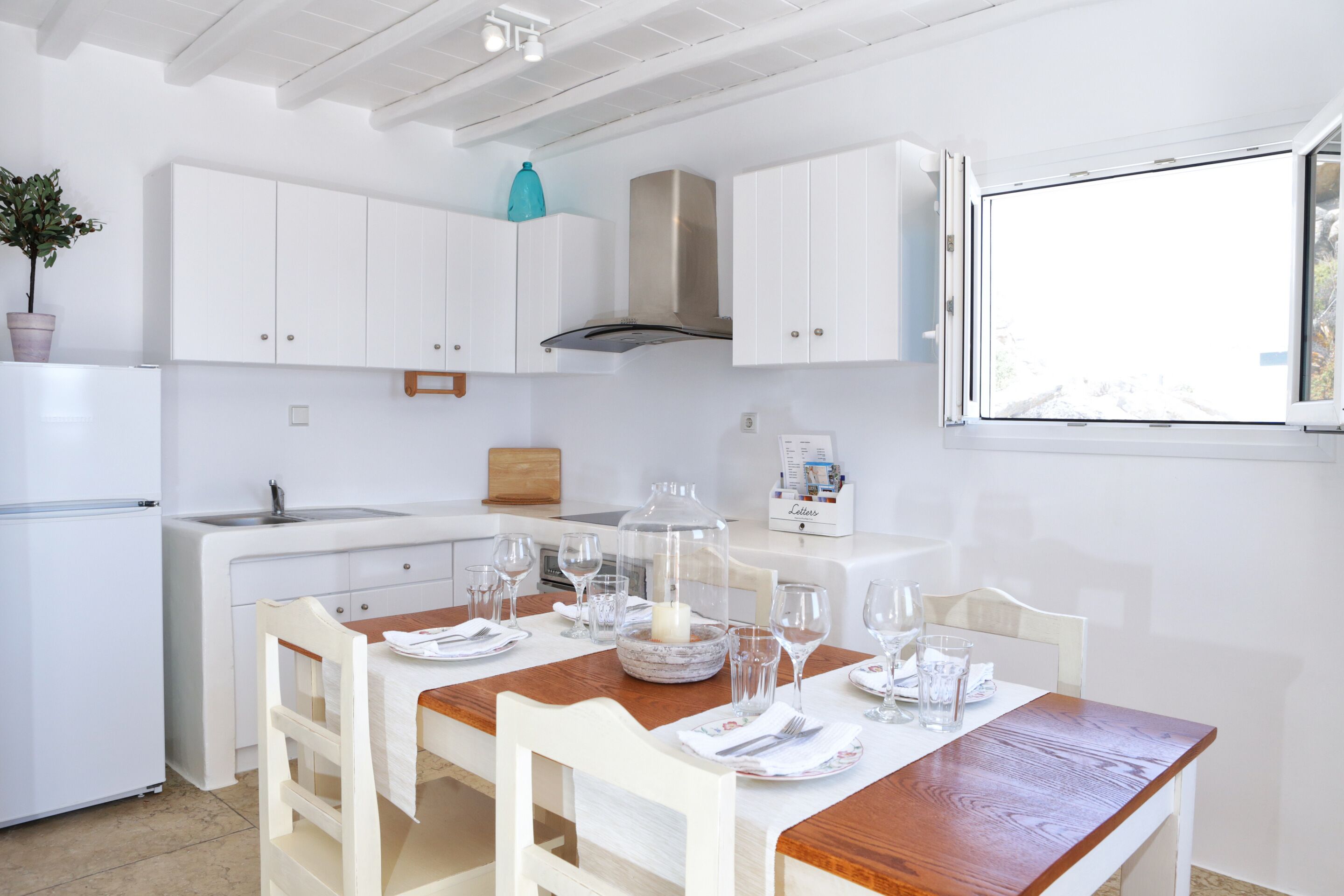 Een moderne keuken met witte kasten, een houten eettafel voor vier personen en een groot raam.