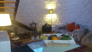 Ein gemütliches Wohnzimmer mit einer Steinsäule, einem Tisch mit Obstkorb, zwei Weingläsern und einer Lampe.