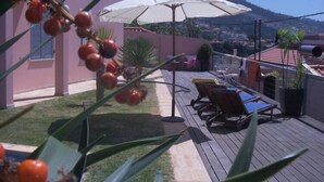 Eine Terrasse mit Lounge-Möbeln und einem weißen Sonnenschirm mit Blick auf eine Wohngegend und Berge.