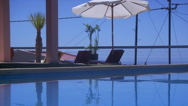 Ein klares Schwimmbecken mit Liegestühlen und Sonnenschirmen, umgeben von Palmen und blauem Himmel.
