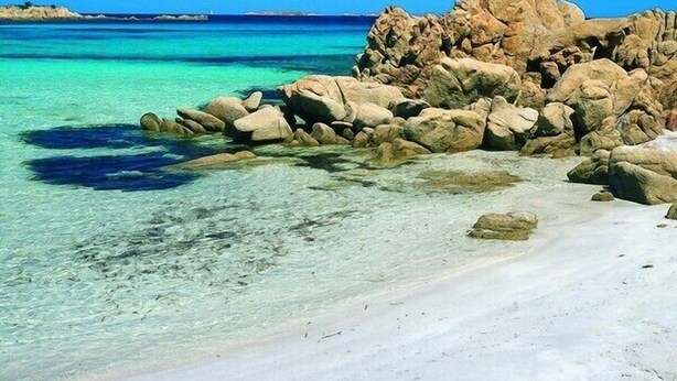 A beach with clear turquoise water, white sand, and large rocks.