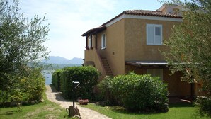 A house with a stone pathway leading to the entrance, surrounded by greenery and a view of the mountains.