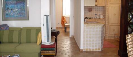 Una sala de estar con un sofá, una mesita y un cuadro enmarcado. Hay una zona de cocina con armarios y un salpicadero de azulejos.