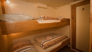 A bunk bed with striped bedding and pillows, a wooden door, and a light fixture on the wall.