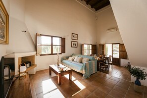 A spacious living room with a sofa, coffee table, and a fireplace. There are multiple windows providing natural light and a view of the outdoors.