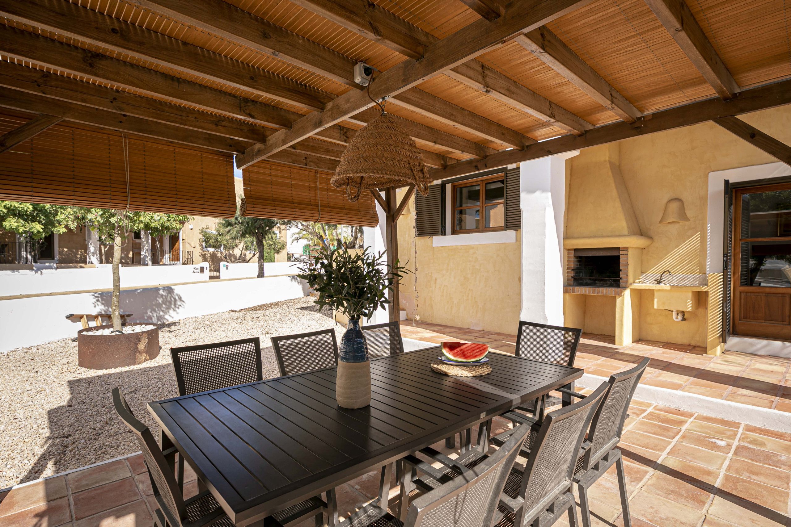 Un patio al aire libre con una mesa y sillas de madera, un colgante de luz y un horno de ladrillo.
