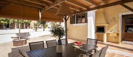 Un patio al aire libre con una mesa y sillas de madera, un colgante de luz y un horno de ladrillo.