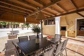 Un patio al aire libre con una mesa y sillas de madera, un colgante de luz y un horno de ladrillo.