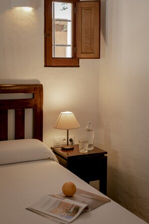 Un dormitorio con una cama, una mesita de noche, una lámpara, una botella y una revista.