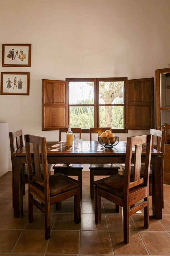 A dining area with a wooden table, chairs, and a window with a view of trees. - Well-equipped house with an unbeatable central location (Sant Francesc de Formentera)