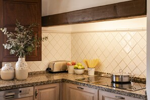 A kitchen with granite countertops, a Siemens dishwasher, a toaster, a bowl of apples, a vase with flowers, and a pot on the stove.